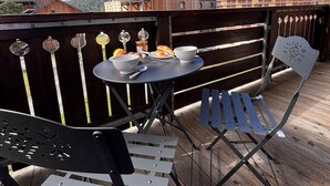 En træterrasse med et bord og stole, med udsigt over et bjerglandskab.