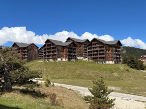 Ein mehrgeschossiges Holzgebäude mit Balkonen, gelegen an einem Hügel unter blauem Himmel.