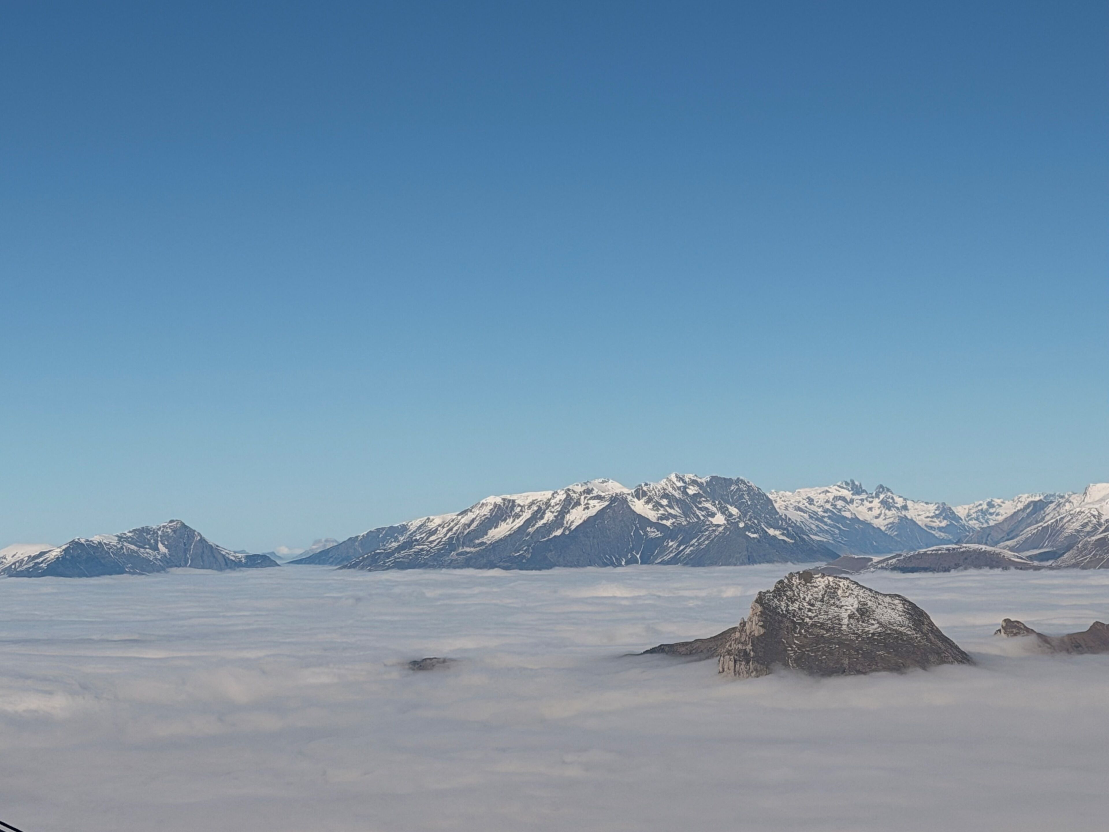 A mountain range with snow-capped peaks and a layer of clouds below.
