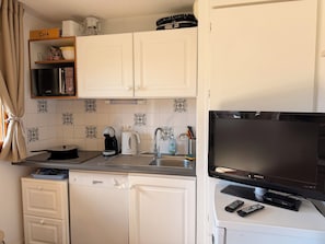 A compact kitchen with white cabinets, a coffee maker, a kettle, a microwave, a dishwasher, and a television. - Cozy haven right on the slopes, chalet vibe and panoramic mountain views (Dévoluy)