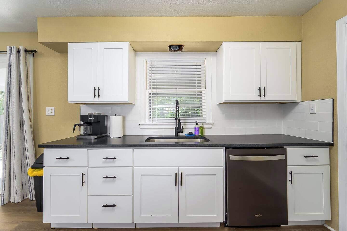 A kitchen with white cabinets, a black countertop, a coffee maker, and a dishwasher.