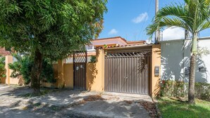 A gated entrance with a metal gate, a concrete driveway, and a palm tree. - Mansão-7quartos em Porto de Galinhas-165 (Camela)