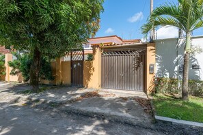 A gated entrance with a metal gate, a concrete driveway, and a palm tree. - Mansão-7quartos em Porto de Galinhas-165 (Camela)