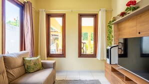 A living room with a sofa, a flat-screen TV, and two windows with curtains. - Mansão-7quartos em Porto de Galinhas-165 (Camela)