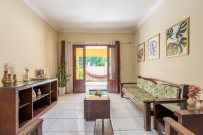 A living room with a sofa, a coffee table, and a TV stand. There is a door leading to an outdoor area. - Mansão-7quartos em Porto de Galinhas-165 (Camela)