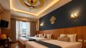 A hotel room with two beds, a wooden floor, a ceiling fan, a TV, and a window with curtains. - Hotel Sangayling  (Paro)