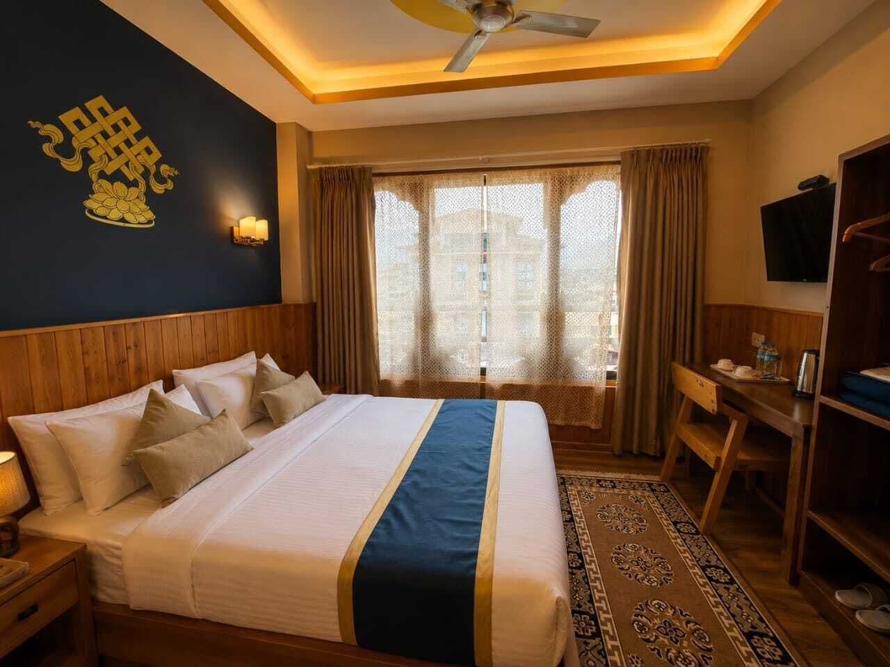 Une chambre d’hôtel comprenant un lit, une table de chevet, une lampe, une télévision, un bureau, une chaise et des rideaux.