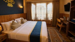 A hotel room with a bed, bedside table, lamp, TV, desk, chair, and curtains. - Hotel Sangayling  (Paro)