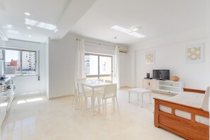 A modern, well-lit room with a dining table, chairs, a TV, and a bed. - Superior 2-Bedroom Apartment – Garden View with Shared Pool (Portimão)
