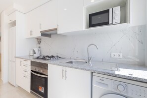 Een moderne keuken met witte kasten, een roestvrijstalen spoelbak, een ingebouwde magnetron, een gasfornuis en een vaatwasser.