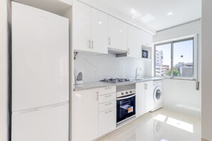 A modern kitchen with white cabinets, a built-in oven, a microwave, and a washing machine. - Superior 2-Bedroom Apartment – Garden View with Shared Pool (Portimão)