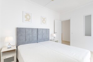 A bedroom with a bed, two bedside tables, a nightstand, a lamp, and two framed pictures on the wall. - Superior 2-Bedroom Apartment – Garden View with Shared Pool (Portimão)