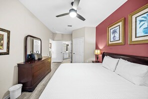 Quarto de hotel com cama, penteadeira, espelho, ventoinha no teto e quadros nas paredes.