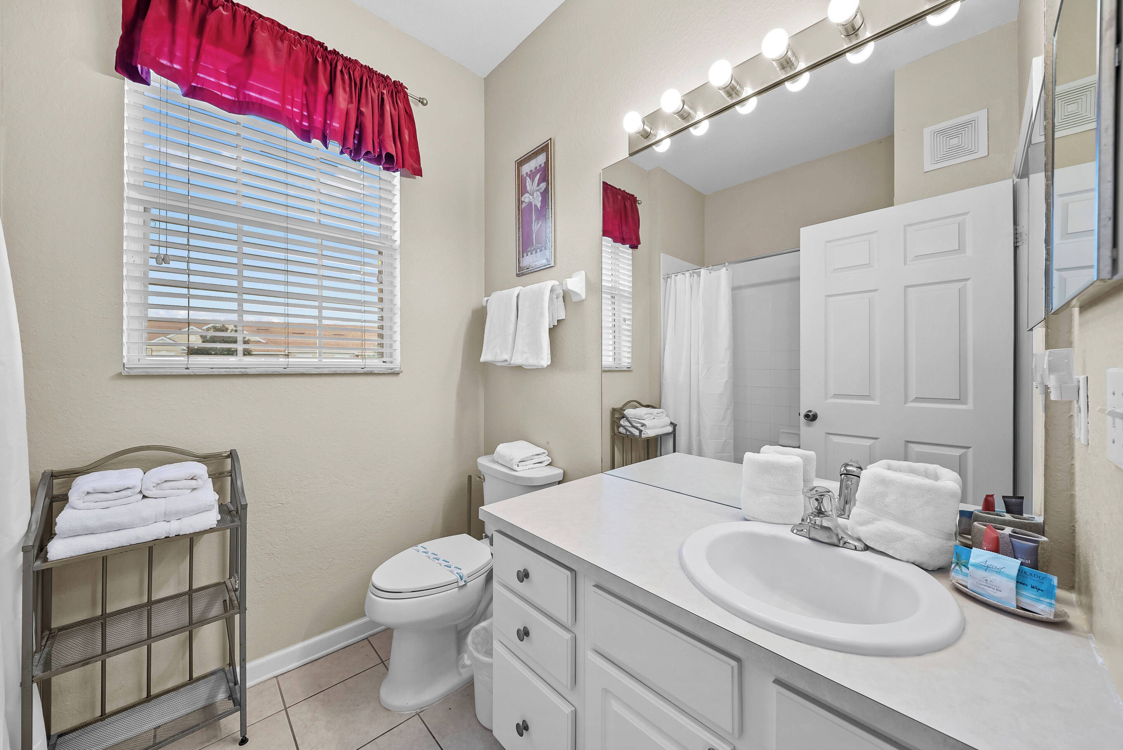 A bathroom with a vanity, sink, toilet, and a window with blinds.