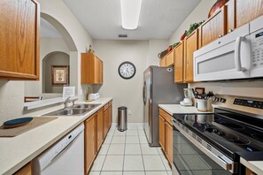 Eine Küche mit Holzausstattung, einem Edelstahlkühlschrank, einer Mikrowelle, einem Backofen und einer Wanduhr.