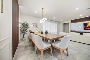 A modern dining area with a wooden table and white chairs, a potted plant, and a ceiling light fixture. - 8BR house with private pool and game room (Clermont)