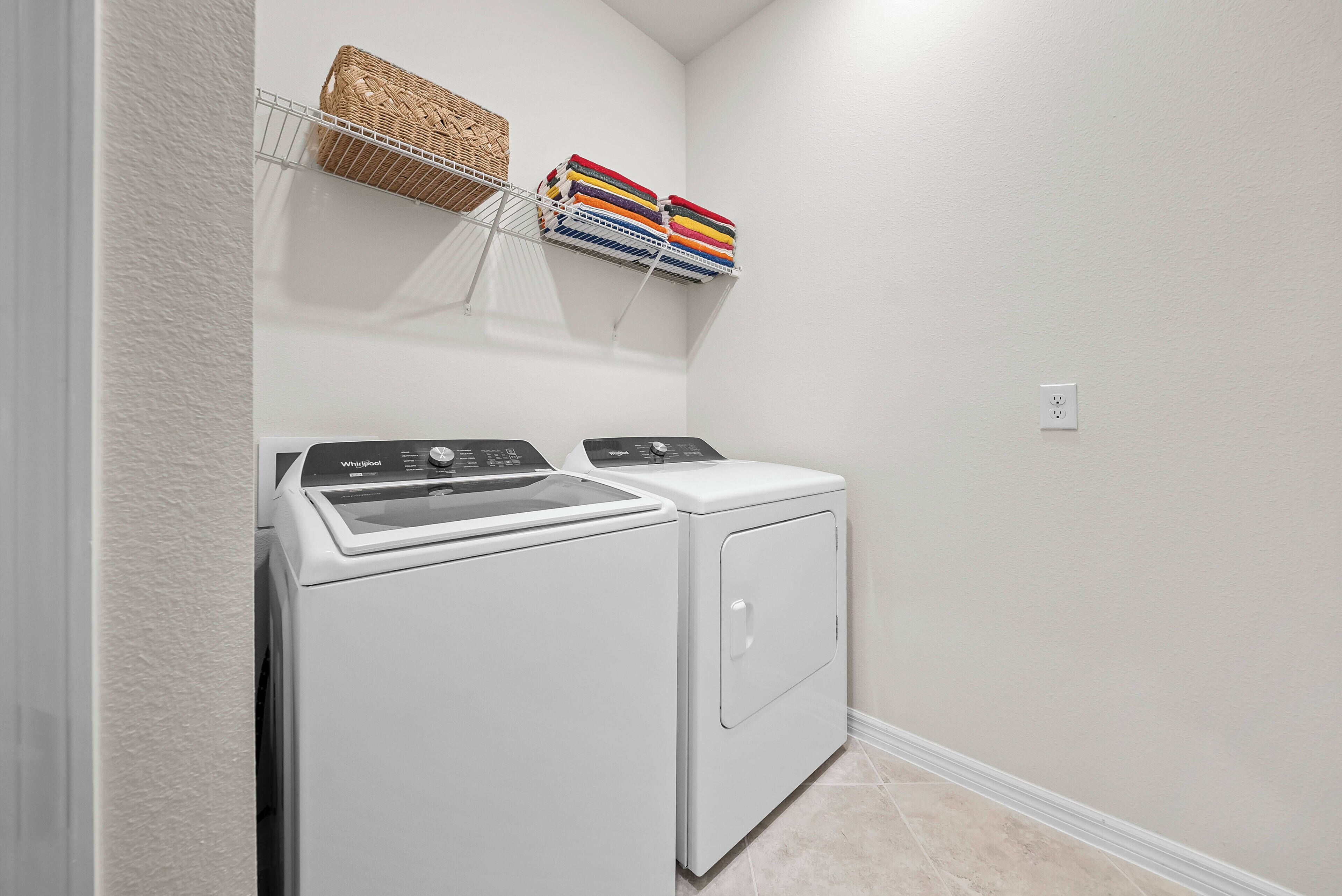 Un espace buanderie comprenant un lave-linge et un sèche-linge à chargement frontal, un panier en osier et un étendoir avec des serviettes pliées.