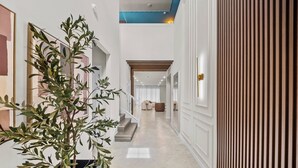 Um corredor com um vaso de planta, um painel de ripas de madeira e uma escada que leva a um quarto com uma porta branca.