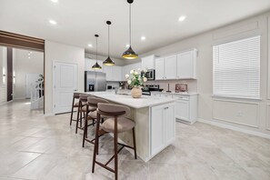 A modern kitchen with a central island, bar stools, pendant lighting, and white cabinetry. - 8BR house with private pool and game room (Clermont)
