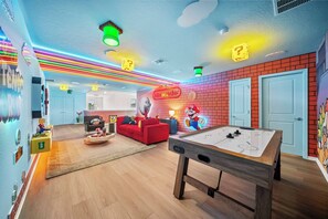 Ein Zimmer mit Billardtisch, einem roten Sofa und dem Nintendo-Logo an der Wand.