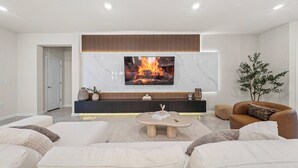 Uma sala de estar moderna com uma televisão de tela plana sobre uma lareira, um sofá de couro marrom e uma poltrona branca.