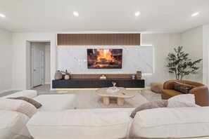 Ein modernes Wohnzimmer mit Flachbildfernseher über einem Kamin, einem braunen Ledersofa und einem weißen Sessel.