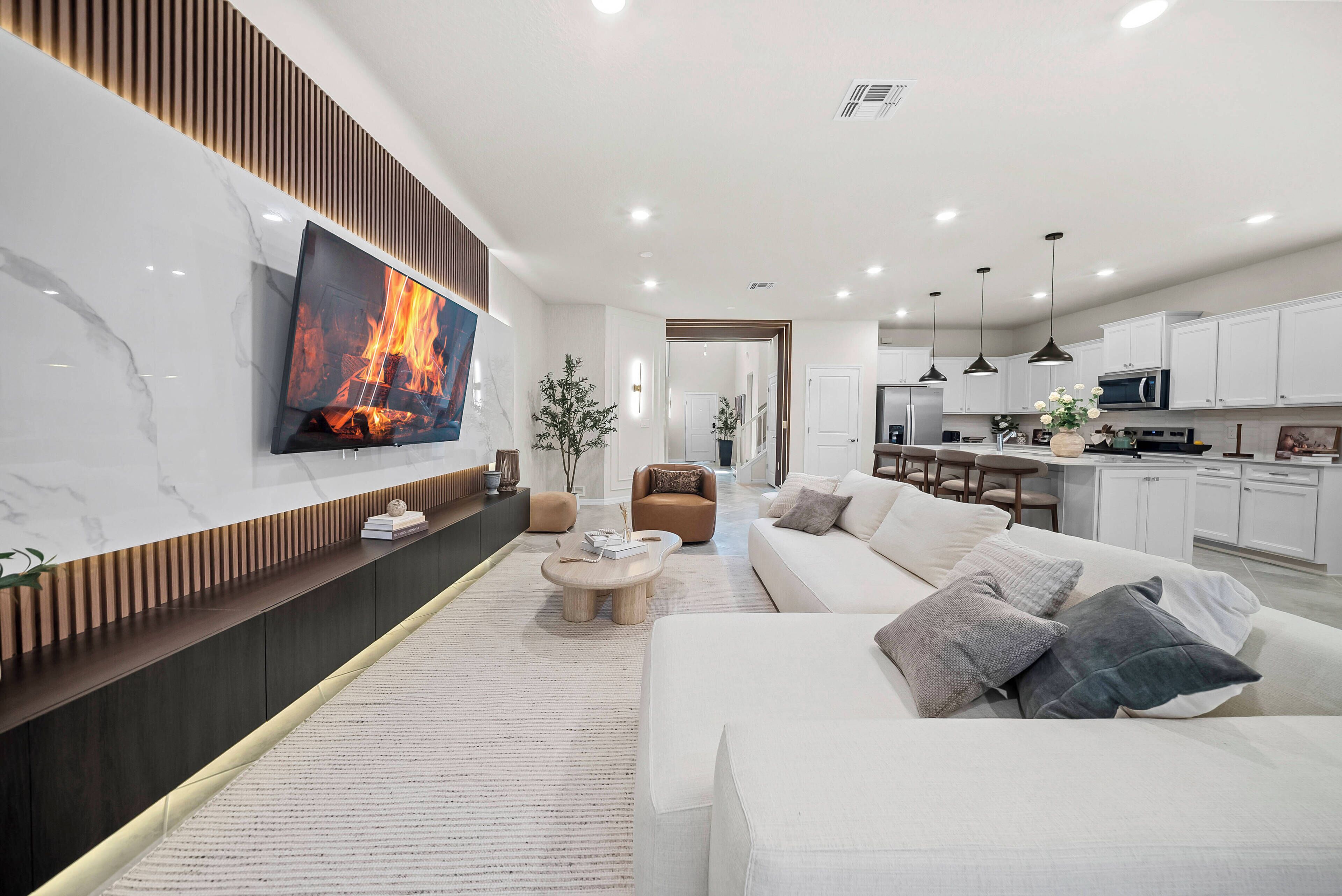A modern living room with a flat-screen TV, a sofa, a coffee table, and a kitchen area with white cabinets and a microwave.