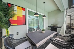 Eine Terrasse im Freien mit Esstisch, Stühlen, Grill und einem großen, abstrakten Gemälde.