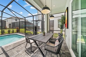 Eine Außenpatio mit Pool, einem Tisch mit Stühlen und einer hängenden Leuchte.