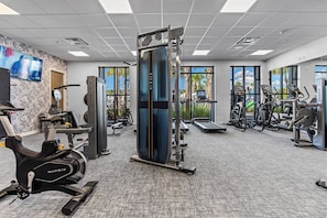 A modern gym with cardio machines, weight training equipment, and large windows offering views of palm trees. - 5BR house with private pool in clermont (Clermont)