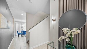 Ein modernes Interieur mit einer Treppe, einem Essbereich mit blauen Stühlen und einem wandmontierten Spiegel.