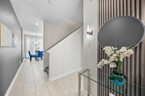 A modern interior with a staircase, a dining area with blue chairs, and a wall-mounted mirror. - 4BR house sleeps 10 with private pool in kissimmee (Kissimmee)