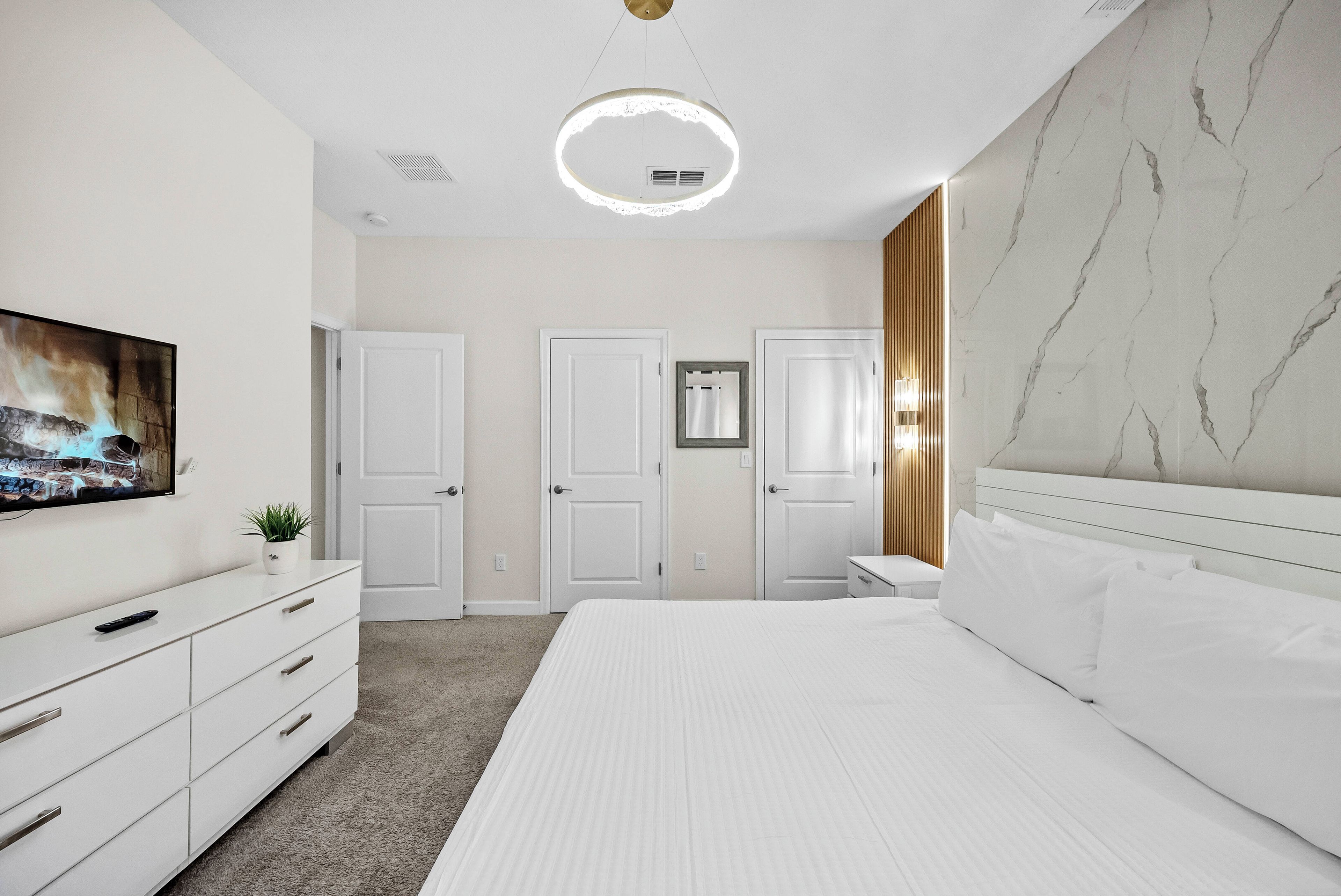 A modern bedroom with a bed, dresser, and a television on the wall.