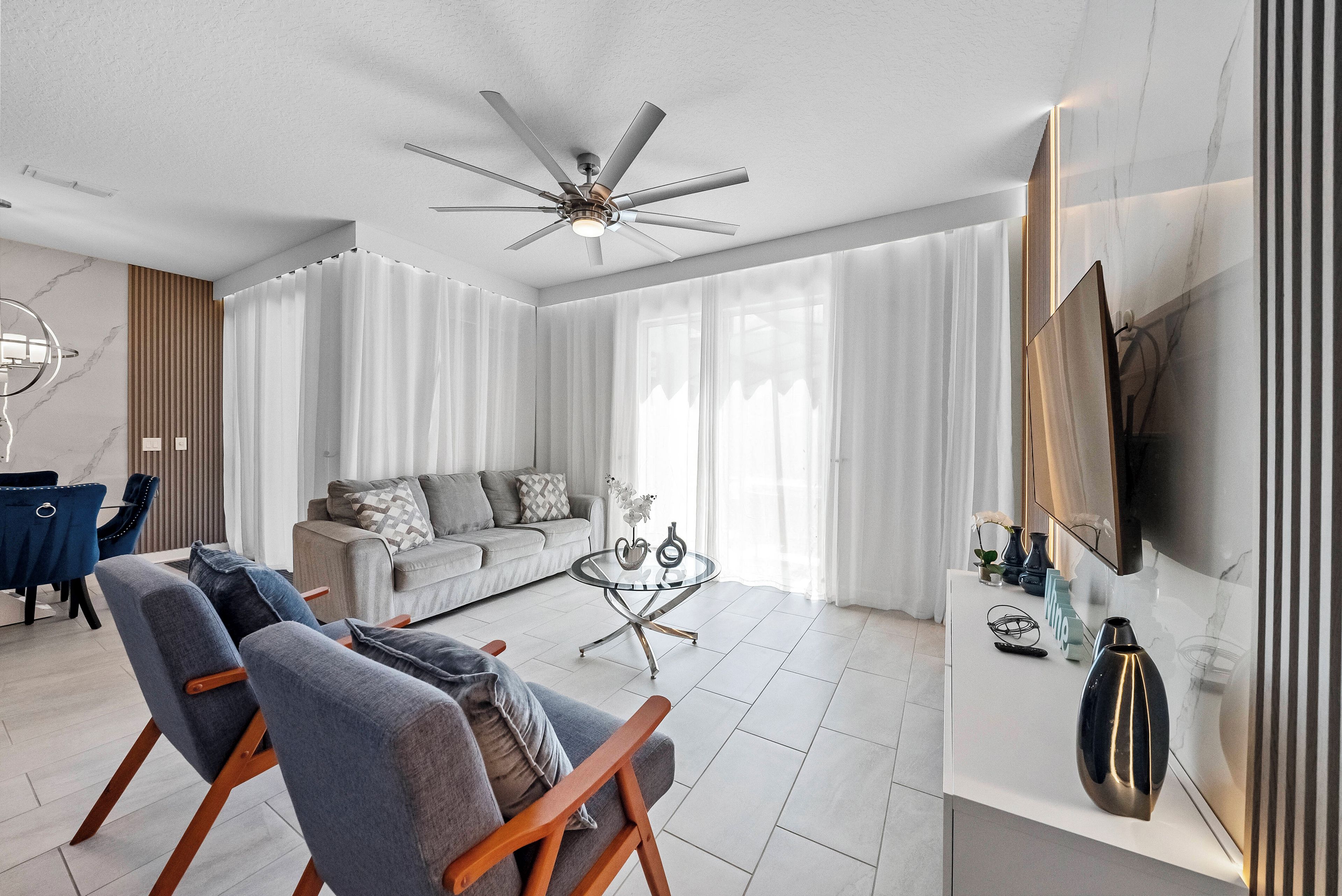 Ein modernes Wohnzimmer mit einer Couch, zwei Sesseln, einem Couchtisch und einem Deckenventilator.
