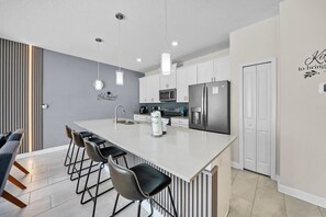 A modern kitchen with a large island, bar stools, a refrigerator, and a microwave. - 4BR house with game room near Disney area (Kissimmee)