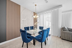 Un espace de salle à manger moderne avec une table en verre entourée de chaises à revêtement bleu, un mur en marbre et un panneau en bois.