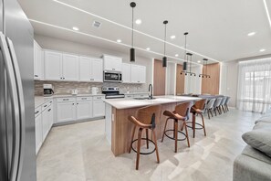 Een moderne keuken met witte kasten, een centraal eiland met barkrukken en hanglampen.