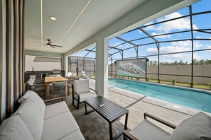 Ein Poolbereich im Freien mit Sitzgelegenheiten, einer Bar und einer großen Leinwand, auf der ein Rennen übertragen wird.