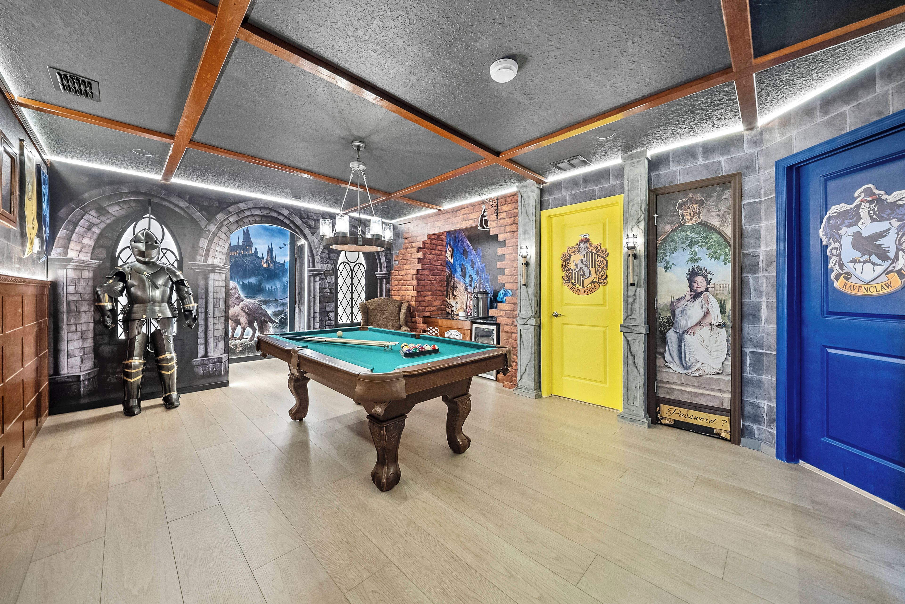 A pool table in a room with a stone wall mural, a yellow door, and a blue door with a crest.