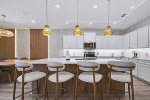 A modern kitchen with white cabinets, a central island with bar stools, and pendant lighting. - 10BR house with private pool and game room (Clermont)