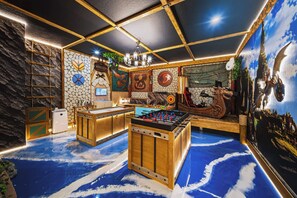 Quarto com mesa de pebolim, bancada de trabalho e um mural de um dragão.
