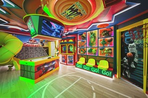 Uma sala de jogos vibrante com tema de basquete, apresentando uma tela grande, diversos jogos eletrônicos e uma área de estar com um letreiro 'Go! Go!'.