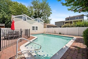 Une piscine résidentielle avec une terrasse en briques, une échelle en métal et une clôture blanche.