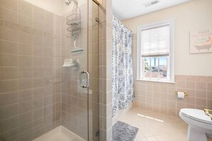 Une salle de bain avec une douche à parois de verre, des toilettes et une fenêtre donnant sur un paysage agréable.