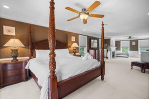 Un lit à baldaquin avec une tête de lit en bois, un ventilateur de plafond et une grande fenêtre dans une chambre.