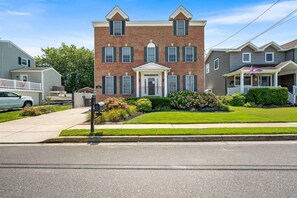 A two-story brick house with a front porch, a mailbox, and a well-maintained lawn. - Haven on Heald | 7BR + Pool Near Beach (Brigantine)