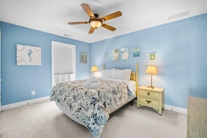 Une chambre à coucher avec un lit, un ventilateur de plafond, une table de chevet et des œuvres d’art murales.