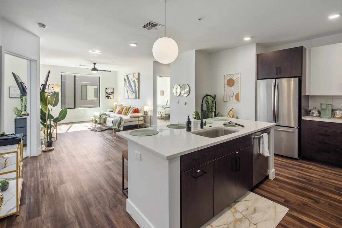 A modern kitchen with a central island, dark cabinetry, stainless steel appliances, and a dining area with a sofa and coffee table.
