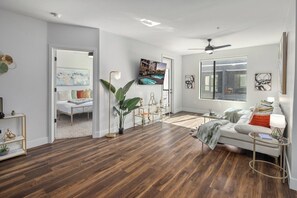 Een ruime woonkamer met een grote bank, een salontafel en een aan de muur bevestigde televisie.