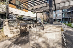 An outdoor patio with a built-in grill and seating area, surrounded by modern buildings. - Escape To The Sage Room 2 BR Suite Tempe Town Lake (Tempe)
